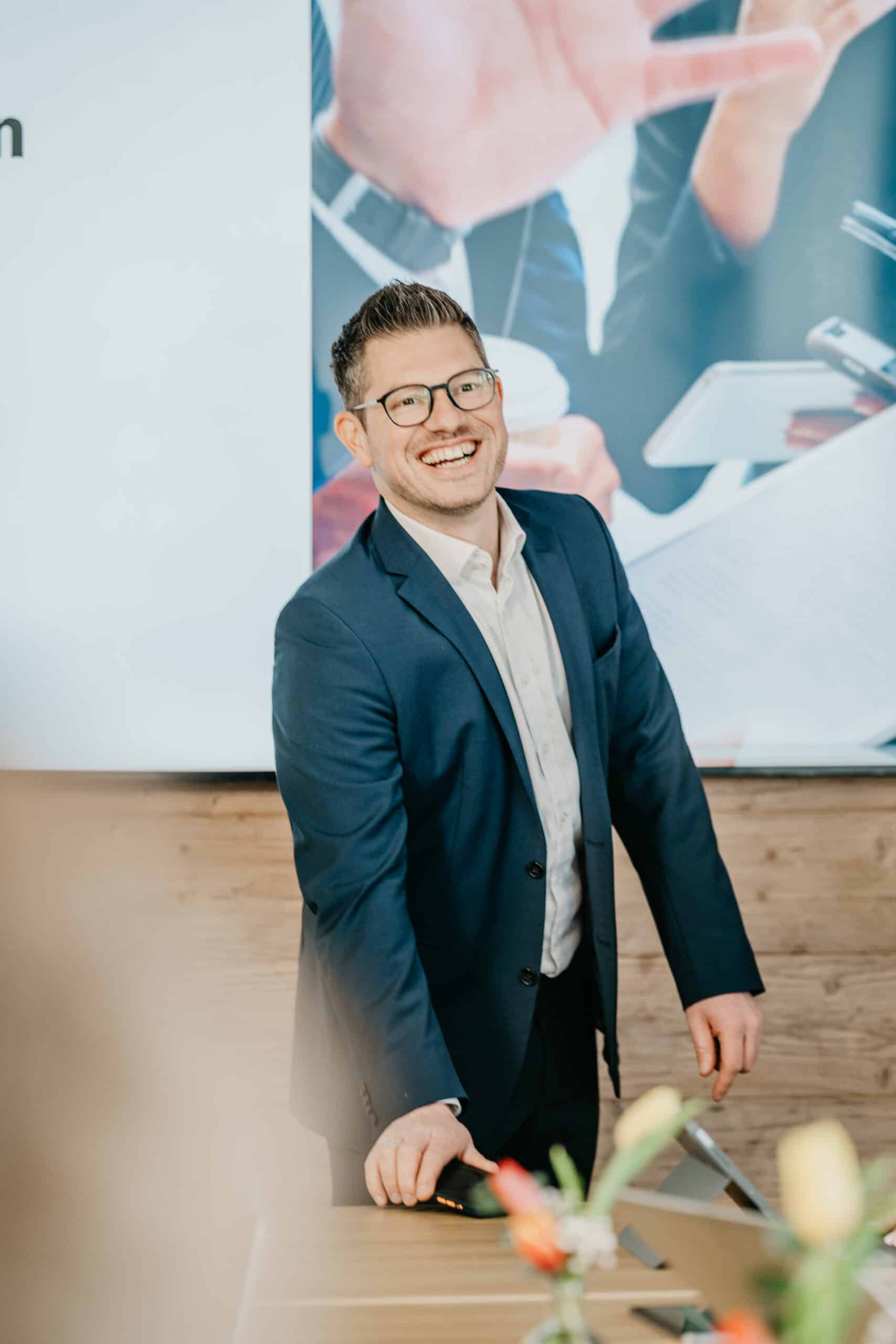 Steuerberater in Business-Kleidung vor Präsentationswand, lächelnd und professionell.