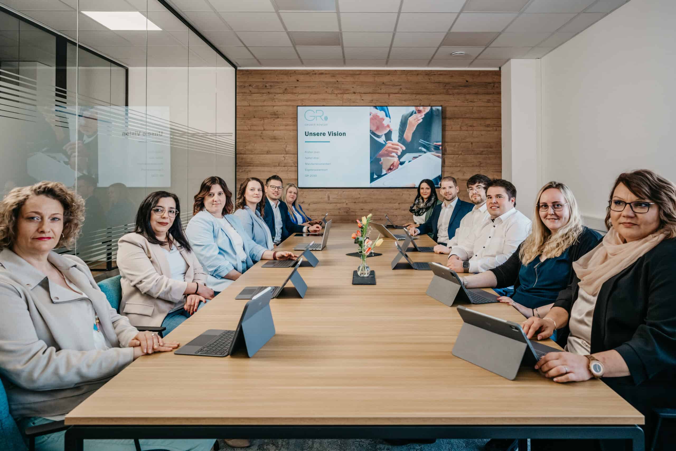 Mitarbeiter bei einer Besprechung im modernen Konferenzraum mit Laptops und Präsentation.