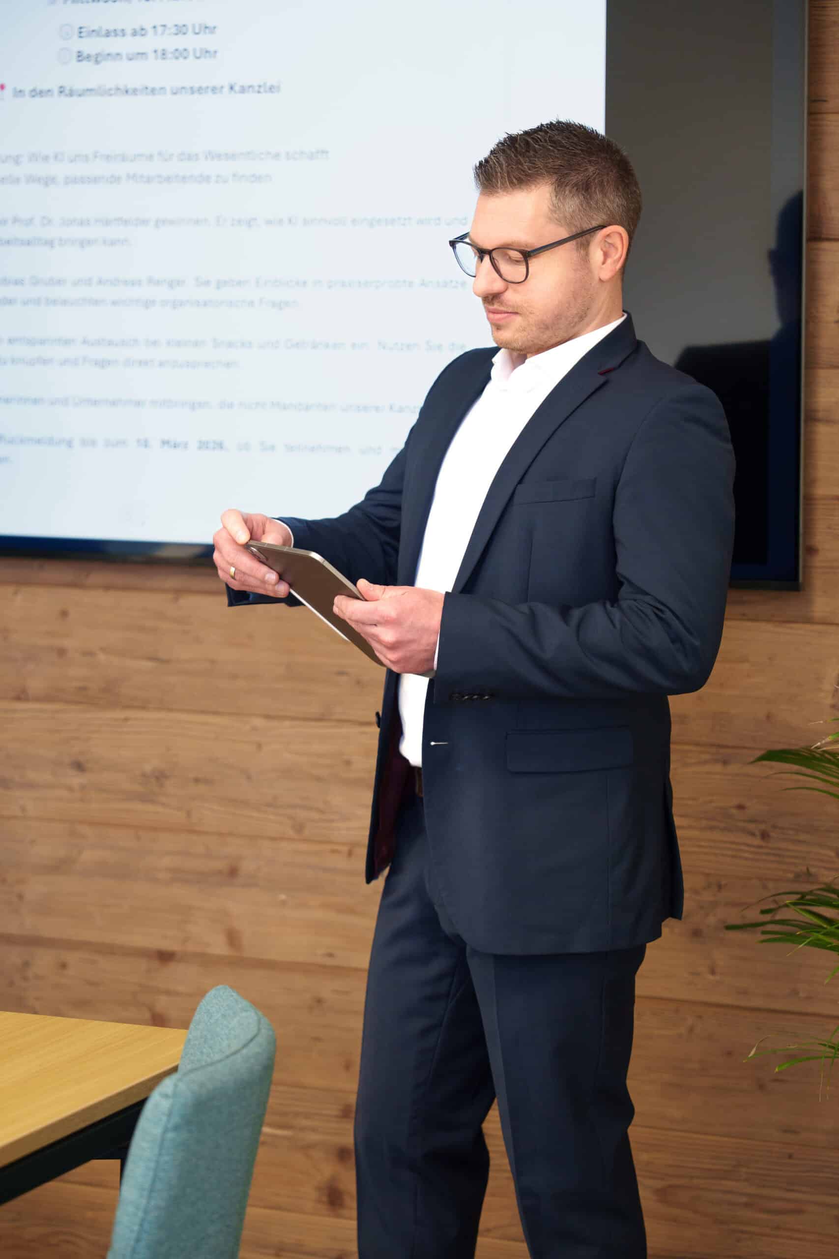 Geschäftsmann in Anzug liest auf einem Tablet während eines Meetings.