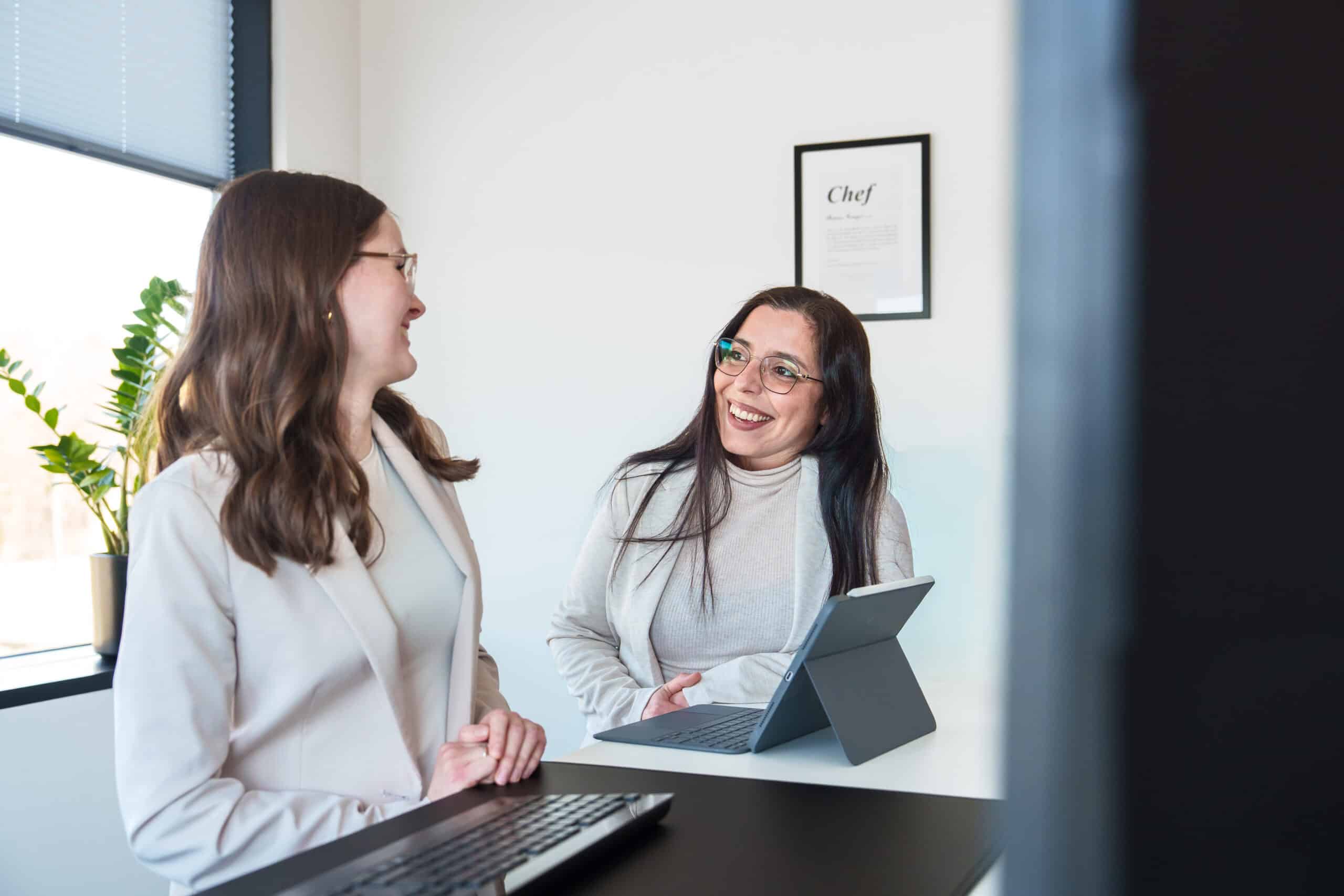 Zwei Frauen im Gespräch in einem modernen Büro, lachen und wirken entspannt.